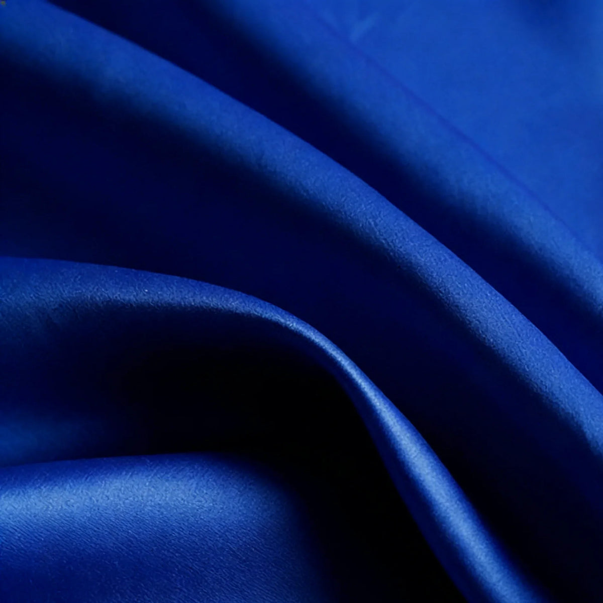 Gros plan sur le Tissu satin mat uni au mètre de Longan Craft France en bleu royal. Sa surface lisse en polyester présente des plis délicats, des ombres douces et une belle brillance - parfaite pour les robes et les vêtements élégants.