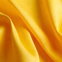 Un gros plan du tissu uni satin mat de Longan Craft France montre des plis jaunes lisses et des ombres douces, mettant en valeur le polyester texturé, idéal pour les robes élégantes et disponible au mètre.