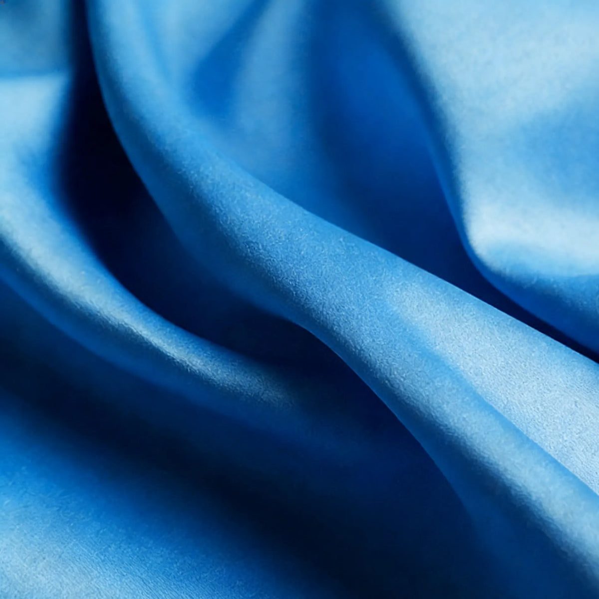 Un gros plan de Tissu satin mat uni au mètre de Longan Craft France révèle sa surface en polyester bleu lisse, doucement pliée et subtilement ombrée, ce qui en fait un produit idéal pour les robes élégantes et les vêtements raffinés.