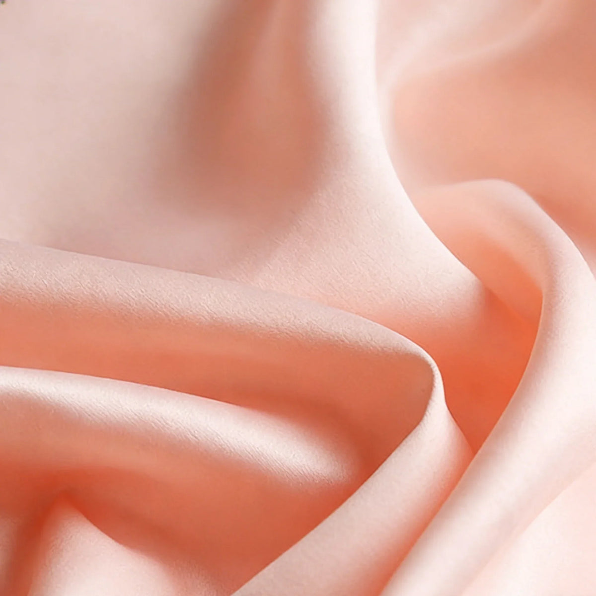 Gros plan sur le Tissu satin mat uni au mètre de Longan Craft France, un satin de polyester rose pêche à la texture lisse et mate et aux plis doux, idéal pour les robes et les vêtements élégants.
