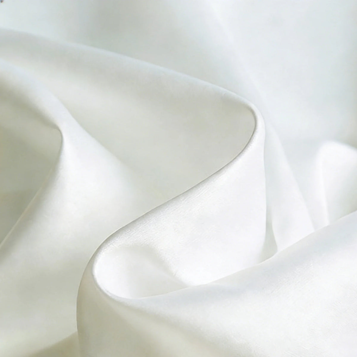 Gros plan sur un tissu satiné blanc mat et lisse de Longan Craft France, révélant des plis doux et une brillance subtile - un textile polyester idéal pour les robes et les vêtements élégants.