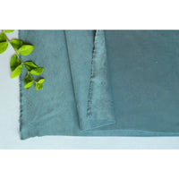 Un morceau de microfibre Matière suédine au mètre de Longan Craft France, aux bords effilochés, est présenté à plat avec un brin de feuille verte dans le coin. Ce tissu doux et extensible dans les quatre sens est idéal pour les projets de bricolage de vêtements.