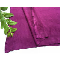 Un morceau de Longan Craft France Matière suédine microfibre au mètre, un tissu violet vif, extensible dans les quatre sens, destiné aux vêtements de bricolage, est posé sur une surface blanche avec, à côté, une branche décorative verte.