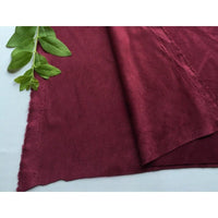 Un morceau de Matière suédine microfibre au mètre de Longan Craft France est posé à plat sur une surface blanche, avec une tige verte feuillue placée dans le coin supérieur gauche du tissu.