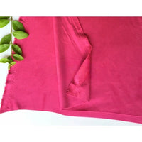 Un morceau de Matière suédine microfibre au mètre rose de Longan Craft France est posé à plat avec un coin plié, révélant les deux côtés. Des feuilles vertes décorent le côté gauche, mettant en valeur ce tissu micro suédine extensible pour vêtements DIY.