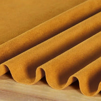 Gros plan sur la Matière suédine microfibre au mètre de Longan Craft France, drapée en plis souples sur une surface en bois. Ce tissu micro suédine lisse et velouté, extensible dans 4 directions, est parfait pour les projets de bricolage de vêtements.