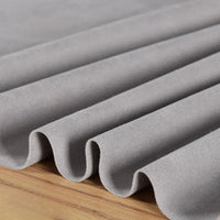 Un gros plan du tissu microfibre suédine de Longan Craft France, drapé en plis souples sur du bois, met en évidence la texture lisse de ce tissu de bricolage gris clair, extensible dans les quatre sens, vendu au mètre.
