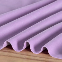 Gros plan sur la Matière suédine microfibre au mètre lilas de Longan Craft France, un tissu doux et extensible dans les quatre sens pour le bricolage, drapé en plis ondulés sur du bois.