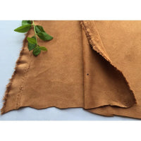Un morceau de Matière suédine microfibre au mètre de Longan Craft France, un tissu micro-suédine extensible dans les 4 sens, de couleur marron clair, destiné aux vêtements de bricolage, est posé à plat avec une tige verte feuillue en haut à gauche. Le fond est blanc uni.