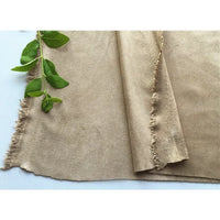 Un morceau de microfibre beige Matière suédine au mètre de Longan Craft France, aux bords effilochés, est posé à plat à côté d'une petite branche verte feuillue sur une surface blanche.