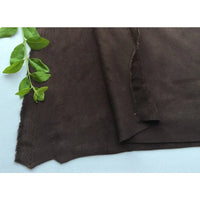 Un morceau de Matière suédine microfibre au mètre de Longan Craft France, un tissu doux et extensible dans les quatre sens pour les vêtements de bricolage, est posé à plat sur une surface blanche avec une branche verte feuillue dans le coin supérieur gauche.