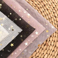 Quatre pièces de Longan Craft France "Tissu tulle lune et étoiles au mètre" en noir, blanc, rose et lavande avec des paillettes étoiles et lune dorées sont empilées sur un tapis, mettant en valeur le tulle multicolore vibrant idéal pour les costumes.