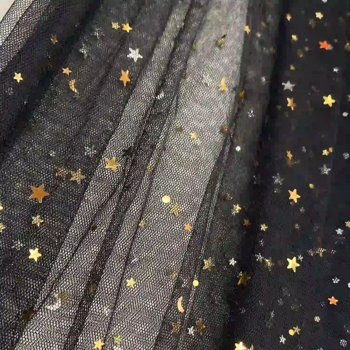 Le Tissu tulle lune et étoiles au mètre de Longan Craft France est un tulle noir multicolore pailleté, orné d'étoiles dorées et argentées, de pois et de croissants de lune. Idéal pour les costumes de scène ou la confection de robes.