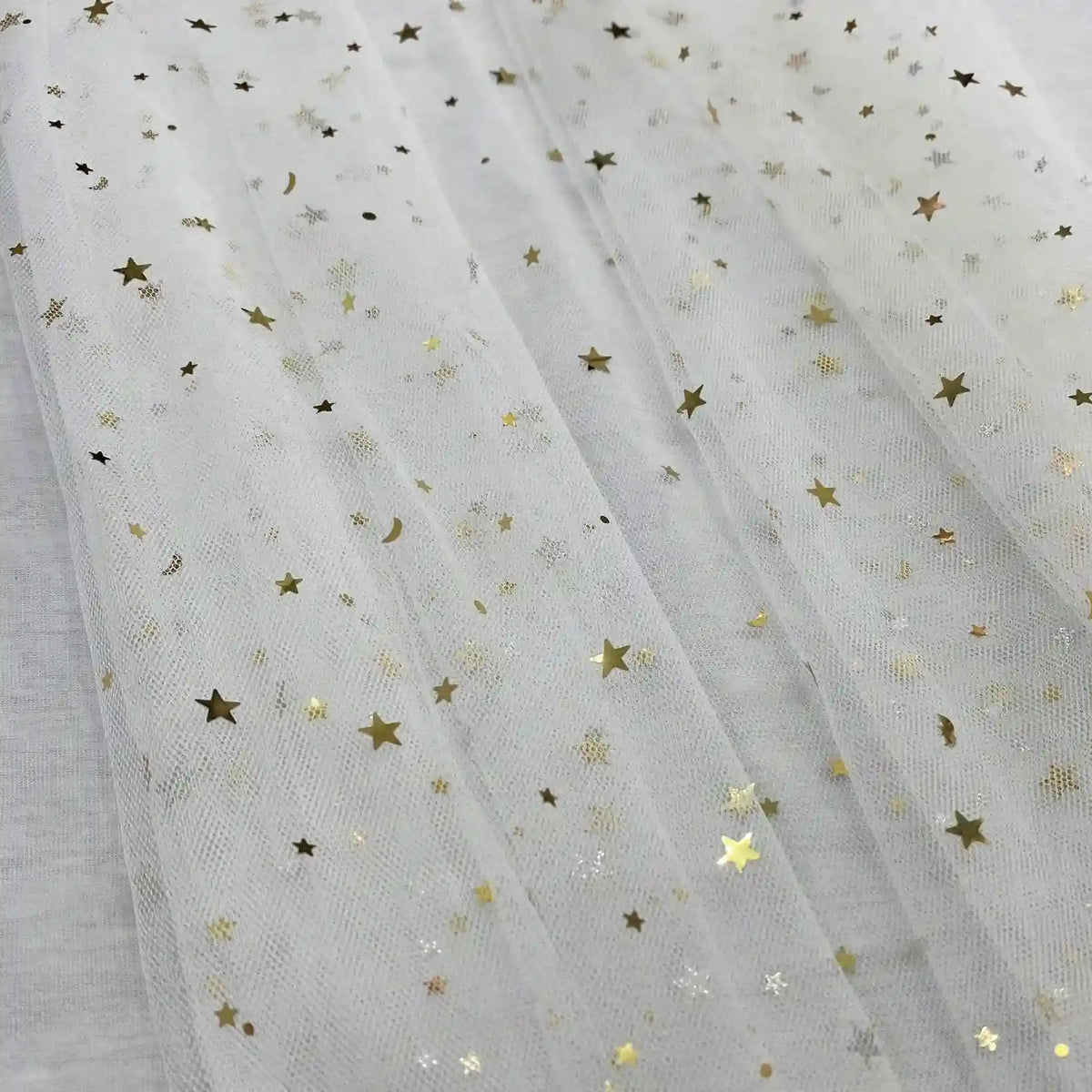 Le Tissu tulle lune et étoiles au mètre de Longan Craft France est un tulle transparent pailleté multicolore avec de délicats motifs d'étoiles et de lunes dorées, parfait pour les costumes de scène, présenté ici à plat en plis souples et translucides.