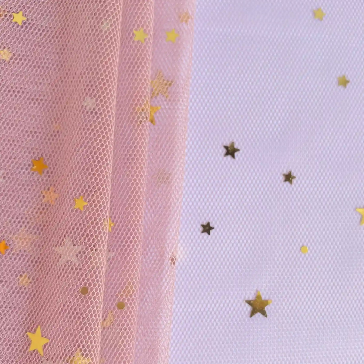 Un morceau de Tissu tulle lune et étoiles au mètre de Longan Craft France repose sur une surface blanche, avec des confettis d'étoiles dorées dispersés à droite. Ce tissu de tulle pailleté multicolore est parfait pour les costumes de scène.