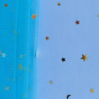 Le Tissu tulle lune et étoiles au mètre de Longan Craft France, un filet bleu avec des paillettes multicolores et des étoiles or/noires, est présenté sur une surface texturée blanche, avec des confettis éparpillés sur le tulle et le fond.