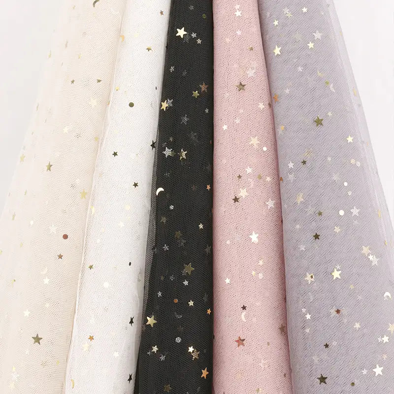 Cinq pièces de Tissu tulle lune et étoiles au mètre de Longan Craft France en beige, blanc, noir, rose et gris clair sont suspendues côte à côte, chacune ornée d'étoiles et de lunes en or métallique - idéal pour les costumes ou les décors.
