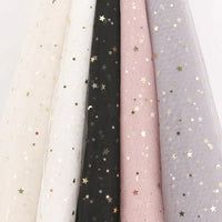 Cinq pièces de Tissu tulle lune et étoiles au mètre de Longan Craft France en beige, blanc, noir, rose et gris clair sont suspendues côte à côte, chacune ornée d'étoiles et de lunes en or métallique - idéal pour les costumes ou les décors.
