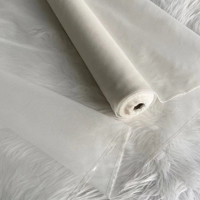 Un rouleau d'Organza de soie multicolore 8 momme de Longan Craft France est déroulé sur une surface blanche duveteuse, mettant en valeur sa légèreté, sa pure soie de mûrier translucide et ses bords finis - un tissu luxueux pour les robes.
