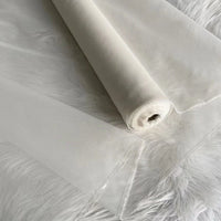Un rouleau d'Organza de soie multicolore 8 momme de Longan Craft France est déroulé sur une surface blanche duveteuse, mettant en valeur sa légèreté, sa pure soie de mûrier translucide et ses bords finis - un tissu luxueux pour les robes.