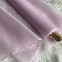 Un rouleau d'Organza de soie multicolore 8 momme de Longan Craft France est déroulé sur une surface blanche et douce. Ce tissu de soie de mûrier, luxueux et léger, révèle subtilement la texture du dessous grâce à sa translucidité.