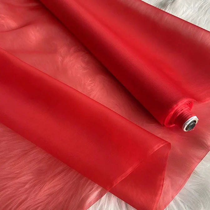 Un rouleau d'organza de soie multicolore 8 momme de Longan Craft France, fabriqué à partir de pure soie de mûrier, est partiellement déroulé sur une surface texturée blanche, mettant en valeur sa légèreté et son luxe semi-transparent pour les robes.