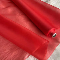 Un rouleau d'organza de soie multicolore 8 momme de Longan Craft France, fabriqué à partir de pure soie de mûrier, est partiellement déroulé sur une surface texturée blanche, mettant en valeur sa légèreté et son luxe semi-transparent pour les robes.