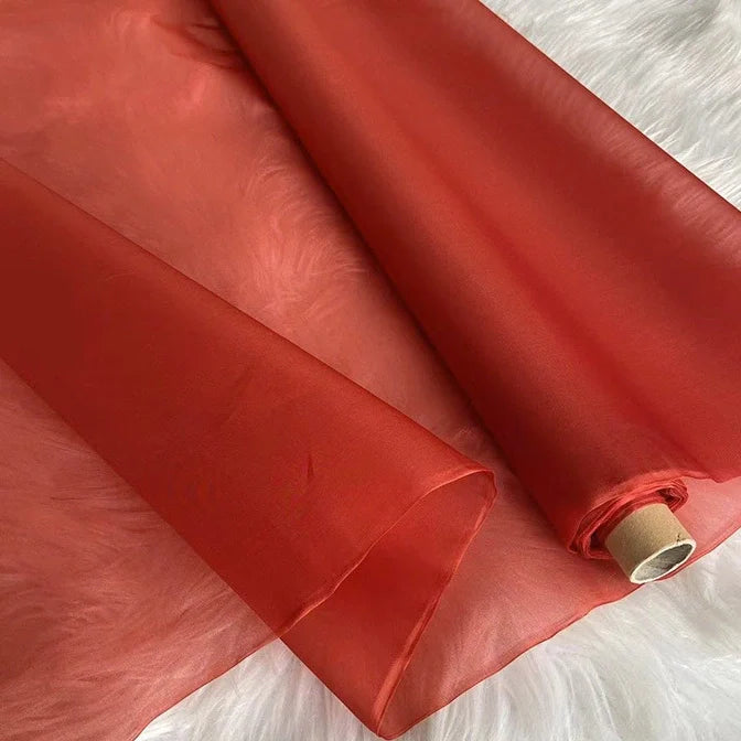 Un rouleau de Longan Craft France Organza de soie multicolore 8 momme, tissu vestimentaire de luxe en pure soie de mûrier, est déroulé sur une surface texturée blanche, mettant en valeur ses qualités de transparence et de légèreté.