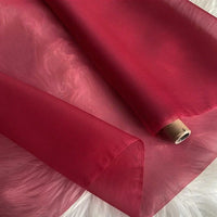 Un rouleau d'Organza de soie multicolore 8 momme au mètre de Longan Craft France, fabriqué à partir de pure soie de mûrier, est étalé sur une douce surface blanche. Le tissu luxueux est partiellement déroulé, révélant sa légèreté et sa translucidité.