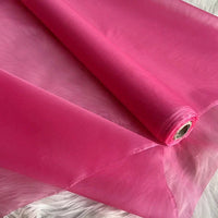 Un rouleau d'Organza de soie multicolore 8 momme de Longan Craft France - un tissu luxueux et transparent en pure soie de mûrier pour les robes - est partiellement déroulé sur une surface texturée blanche, montrant sa qualité lisse, légère et semi-transparente.