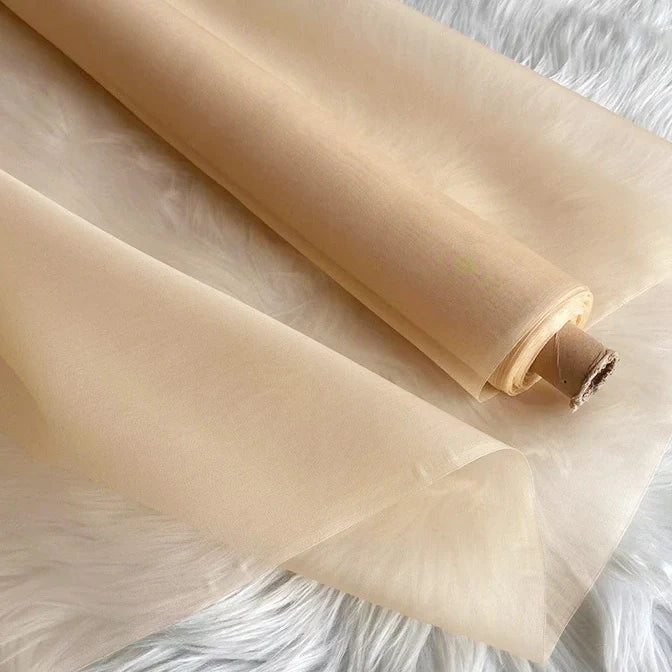 Un rouleau d'Organza de soie multicolore 8 momme de Longan Craft France est partiellement déroulé sur une surface blanche et pelucheuse. Le tissu en pure soie de mûrier semble translucide et lisse, mettant en valeur sa texture luxueuse et délicate, idéale pour les robes élégantes.