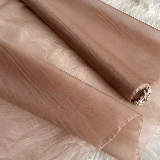 Gros plan sur l'Organza de soie multicolore 8 momme au mètre de Longan Craft France, tissu en pure soie de mûrier, déroulé sur une surface en fourrure blanche ; on voit sa texture diaphane et légèrement brillante ainsi que son extrémité partiellement effilochée.