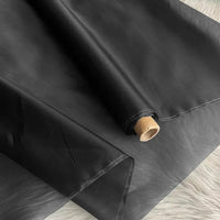 Un rouleau d'Organza de soie multicolore 8 momme de Longan Craft France est partiellement déroulé sur une surface légère, mettant en valeur la texture et l'épaisseur luxueuses de la pure soie de mûrier, avec son âme en carton exposée à une extrémité.
