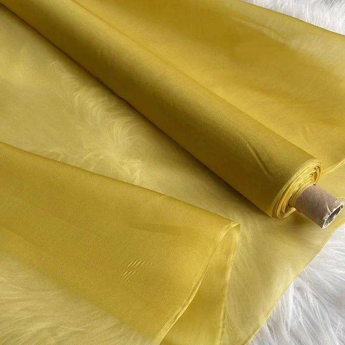 Un rouleau d'Organza de soie multicolore 8 momme de Longan Craft France, fabriqué à partir de pure soie de mûrier, est partiellement déroulé sur une surface texturée blanche, montrant sa finition luxueuse translucide et lisse, idéale pour les robes élégantes.