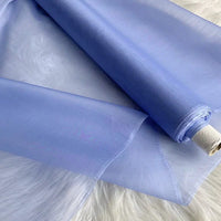 Un rouleau d'"Organza de soie multicolore 8 momme au mètre" de Longan Craft France, tissu de pure soie de mûrier pour robes de luxe, est partiellement déroulé sur une surface blanche. Le tissu de soie apparaît translucide, avec des bords lisses visibles.