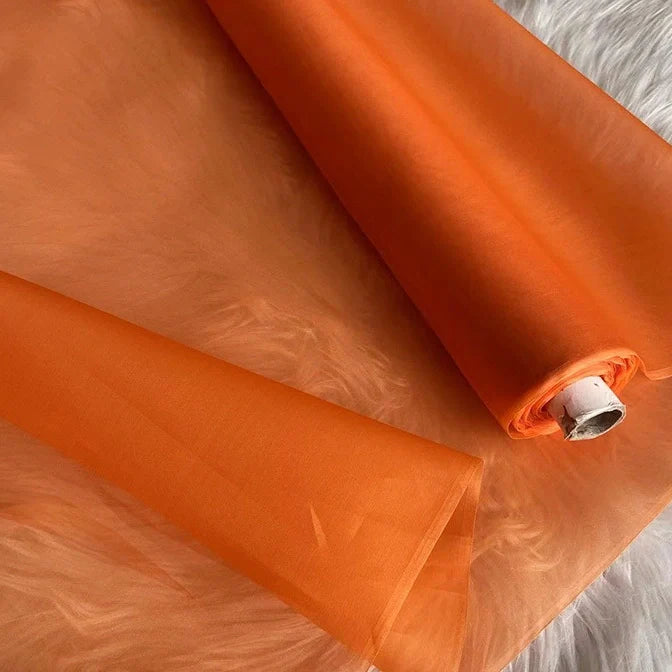 Un rouleau partiellement déroulé d'Organza de soie multicolore 8 momme au mètre de Longan Craft France, un tissu de luxe fin, léger et translucide en pure soie de mûrier pour les robes, est présenté sur une surface blanche et douce.