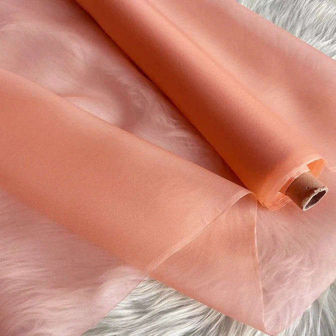 Un rouleau d'Organza de soie multicolore 8 momme de Longan Craft France, fabriqué à partir de pure soie de mûrier, est partiellement déroulé sur une surface blanche, montrant sa luxueuse texture légère et translucide, idéale pour les robes.
