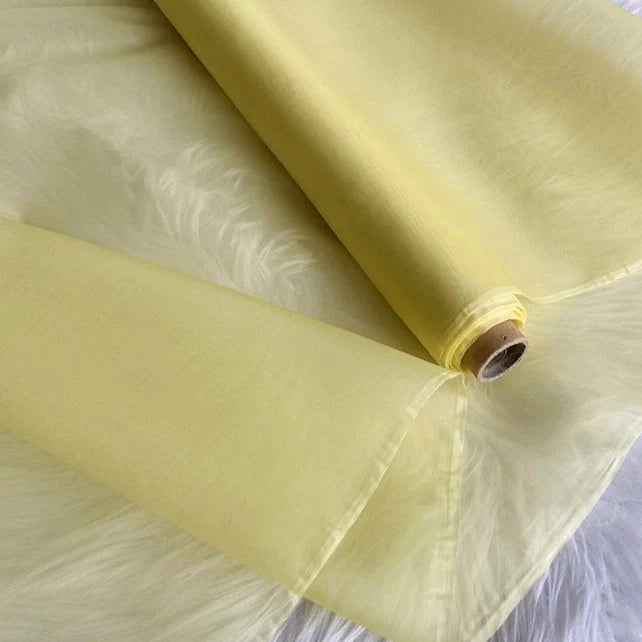 Un rouleau d'Organza de soie multicolore 8 momme de Longan Craft France, fabriqué à partir de pure soie de mûrier, est présenté déroulé sur une surface texturée blanche - son luxe transparent et léger est idéal pour les robes de chambre et les robes de soirée élégantes.