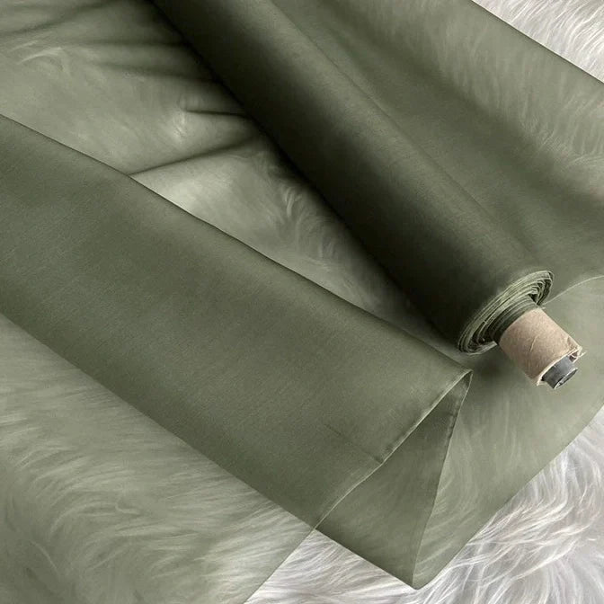 Un rouleau partiellement déroulé d'Organza de soie multicolore 8 momme de Longan Craft France repose sur une surface blanche et duveteuse. Ce tissu en pure soie de mûrier est lisse et semi-transparent, idéal pour la confection de robes luxueuses.