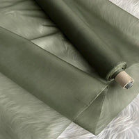 Un rouleau partiellement déroulé d'Organza de soie multicolore 8 momme de Longan Craft France repose sur une surface blanche et duveteuse. Ce tissu en pure soie de mûrier est lisse et semi-transparent, idéal pour la confection de robes luxueuses.