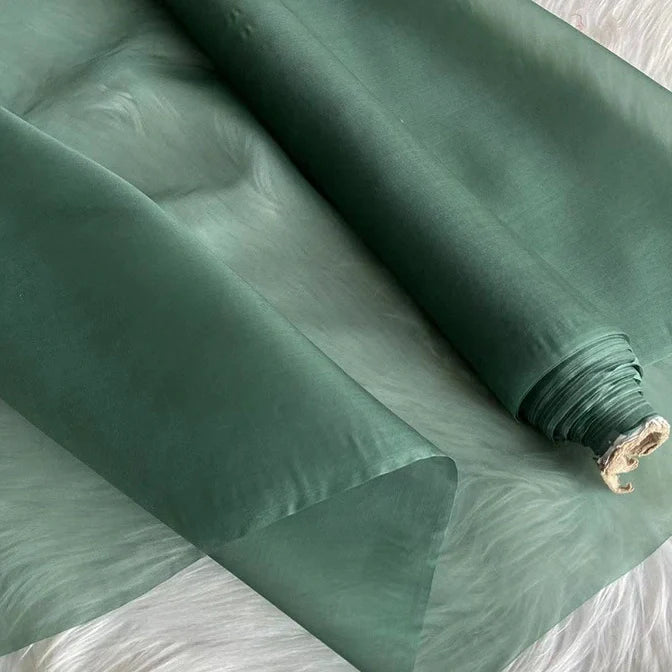 Un rouleau d'Organza de soie multicolore 8 momme au mètre de Longan Craft France, fabriqué à partir de pure soie de mûrier, est partiellement déroulé sur une surface légère, révélant son tissu de luxe lisse et légèrement translucide, idéal pour les robes.
