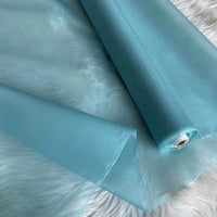 Un rouleau d'Organza de soie multicolore 8 momme de Longan Craft France, fabriqué à partir de pure soie de mûrier, est partiellement déroulé sur une surface blanche duveteuse. Ce tissu luxueux est idéal pour les robes de soirée et les robes élégantes.