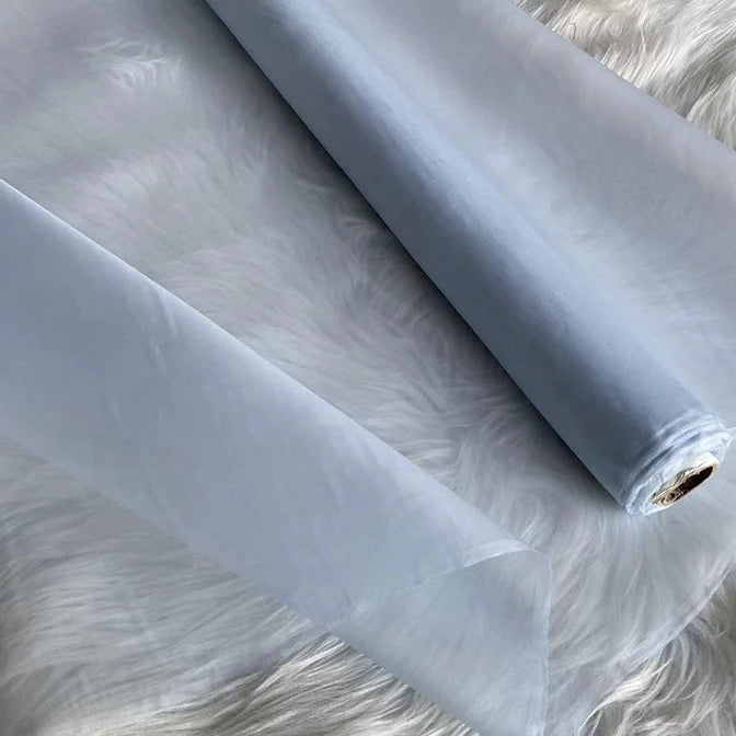 Un rouleau d'Organza de soie multicolore 8 momme au mètre de Longan Craft France, en pure soie de mûrier, est déroulé sur une surface texturée blanche. Ce tissu luxueux, fin et translucide est idéal pour les robes élégantes et les robes du soir.