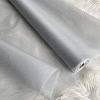 Un rouleau partiellement déroulé d'Organza de soie multicolore 8 momme au mètre (pure soie de mûrier, tissu vestimentaire de luxe) de Longan Craft France est posé sur une surface blanche, sa matière translucide et lisse étant accompagnée d'une autre section similaire.