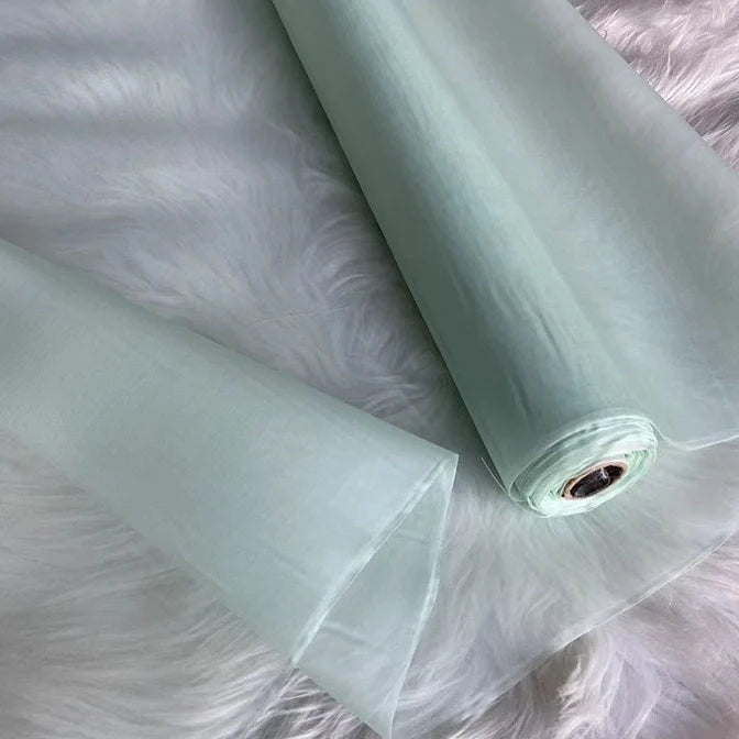 Un rouleau de Longan Craft France Organza de soie multicolore 8 momme, fabriqué à partir de pure soie de mûrier, est déroulé sur une surface blanche. Ce tissu luxueux et translucide est parfait pour la confection de robes de soirée élégantes et de vêtements haut de gamme.