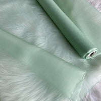 Deux rouleaux d'"Organza de soie multicolore 8 momme au mètre" de Longan Craft France, tissu de luxe en pure soie de mûrier pour robes, sont posés sur de la fausse fourrure blanche.