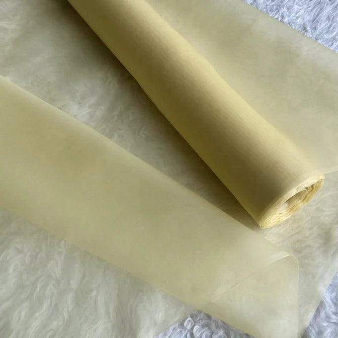 Gros plan sur deux feuilles translucides d'Organza de soie multicolore 8 momme de Longan Craft France, tissu de luxe en pure soie de mûrier pour robes, posées sur une surface blanche texturée.