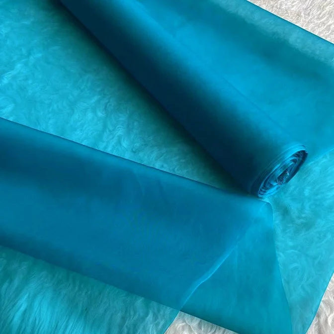 Un rouleau de Longan Craft France Organza de soie multicolore 8 momme au mètre, tissu de pure soie mûrier, est partiellement déroulé pour montrer sa texture luxueuse et translucide, idéale pour créer des robes élégantes.