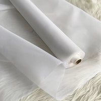 Un rouleau partiellement déroulé d'Organza de soie multicolore 8 momme de Longan Craft France, fabriqué à partir de pure soie de mûrier, est présenté sur une surface blanche et douce. Ce tissu luxueux est léger et translucide, idéal pour les robes élégantes.