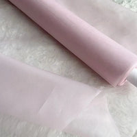 Un rouleau d'Organza de soie multicolore 8 momme au mètre de Longan Craft France, en pure soie de mûrier, est présenté partiellement déroulé sur une surface blanche - sa finition translucide et délicate est parfaite pour les robes de soirée luxueuses.